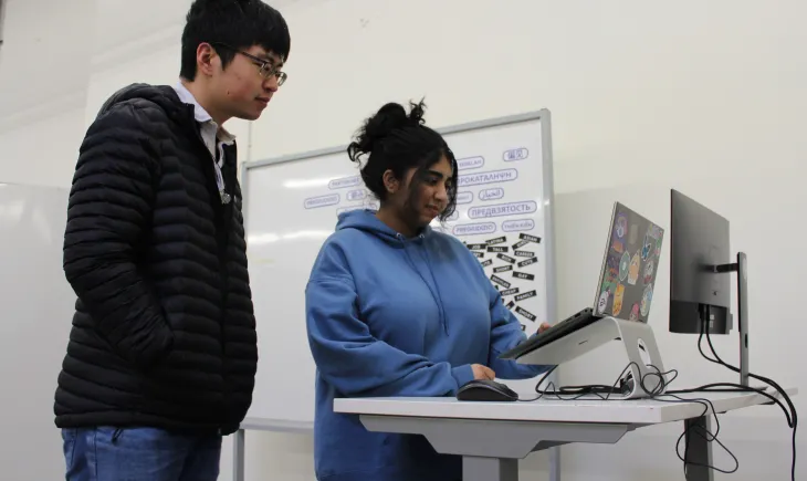 Two students looking at laptop on standing desk